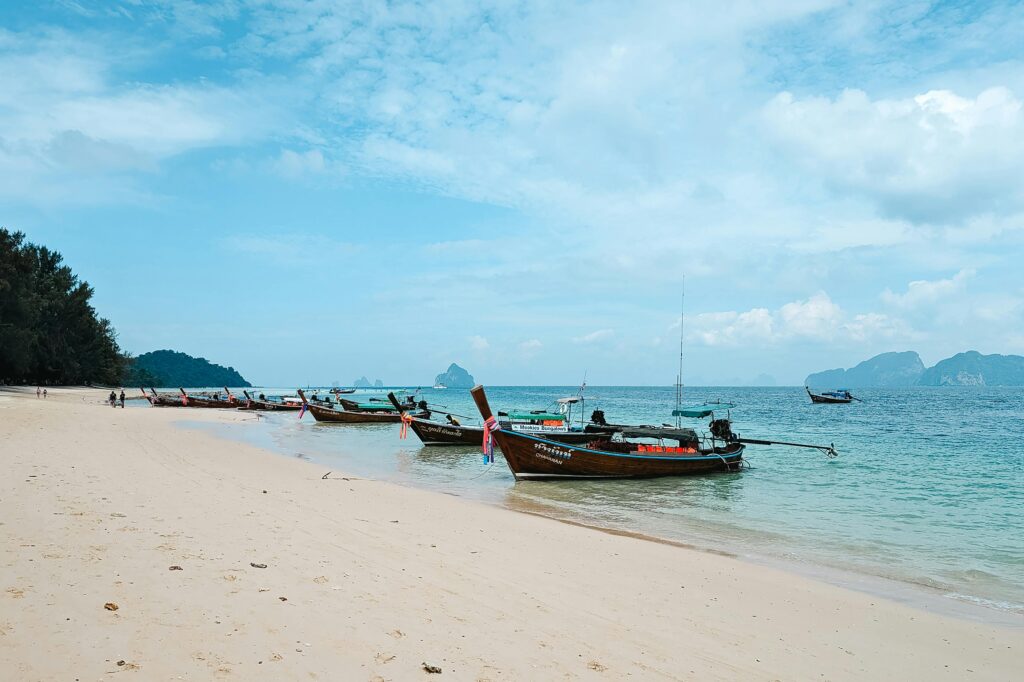 Serene Thai beach scene featuring longtail boats and tropical scenery under a blue sky.
